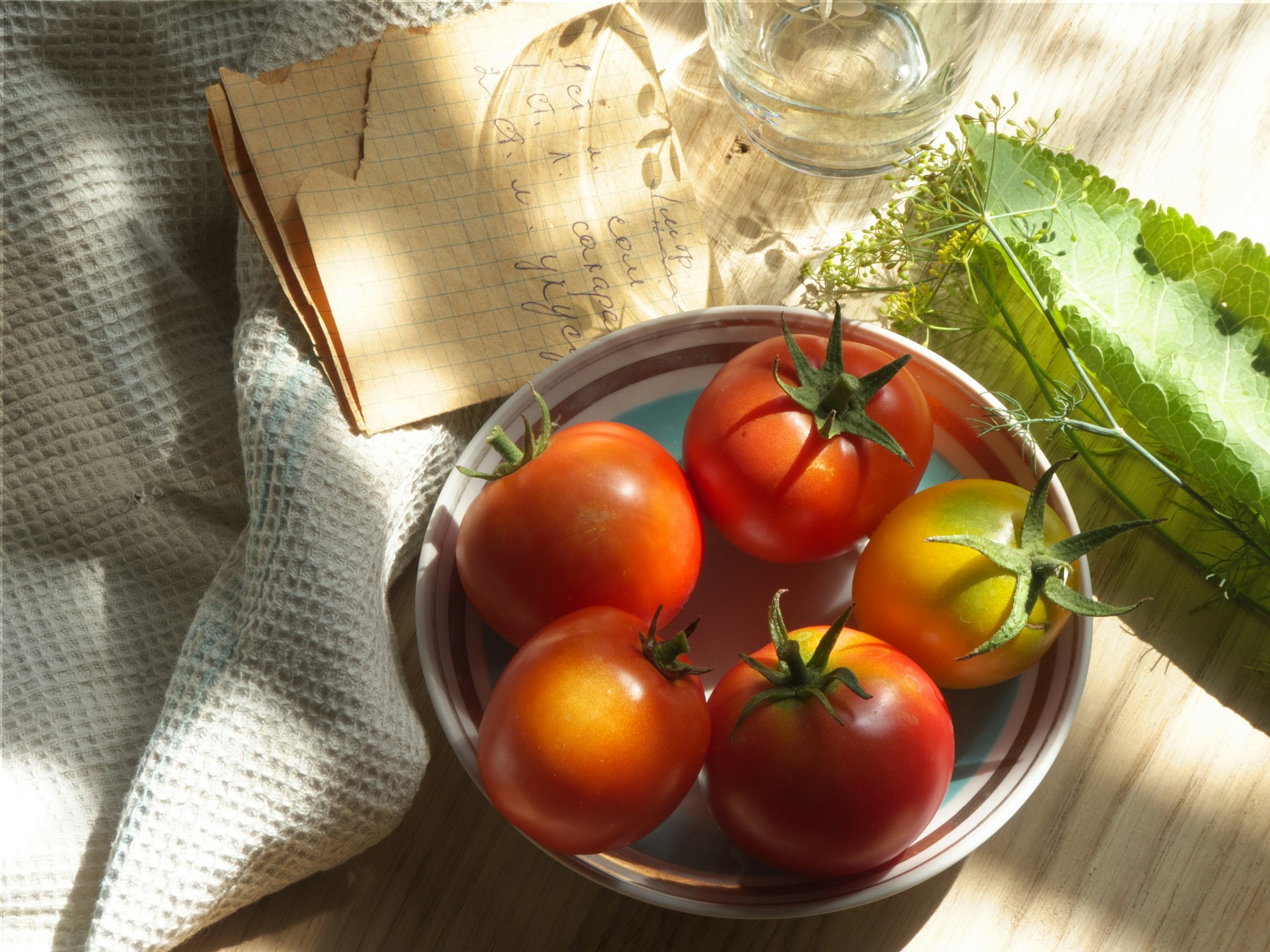 Frische Tomaten in einer Glasschale neben einer handgeschriebenen Notiz und Dill
